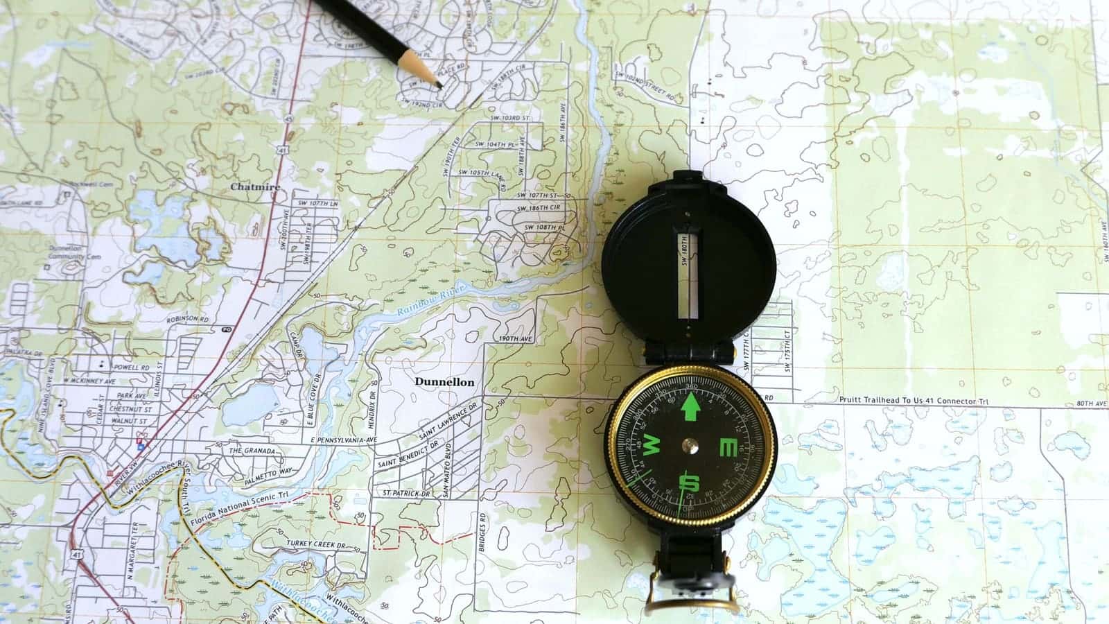 A compass resting on a printed topographic map beside a pencil