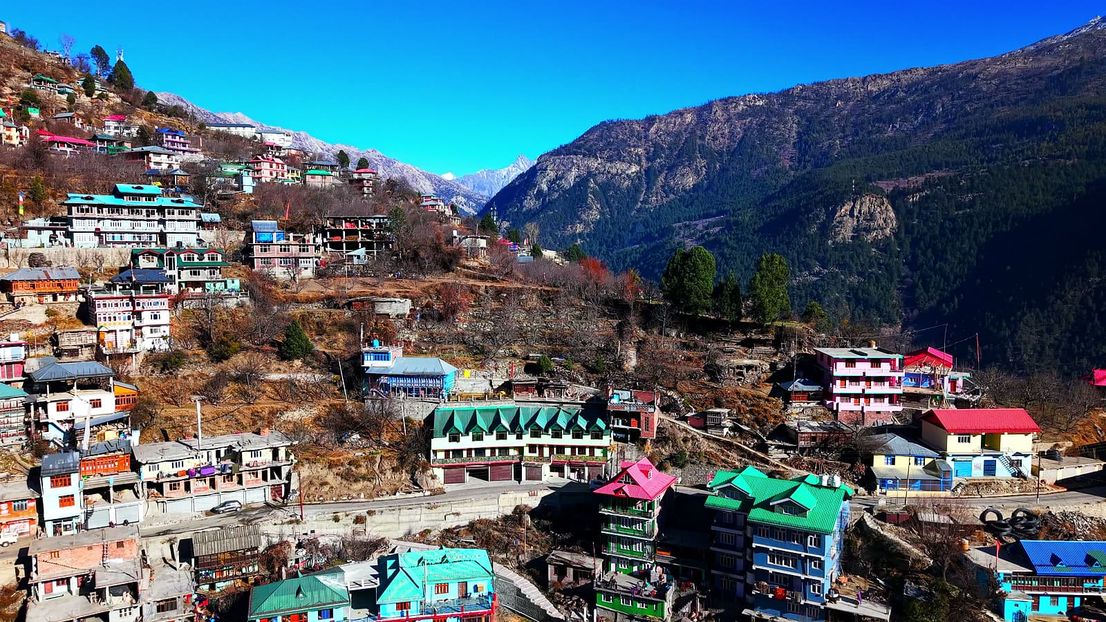 Aerial view of the Pangtu Homestay among colourful houses on a mountain slope under a clear blue sky