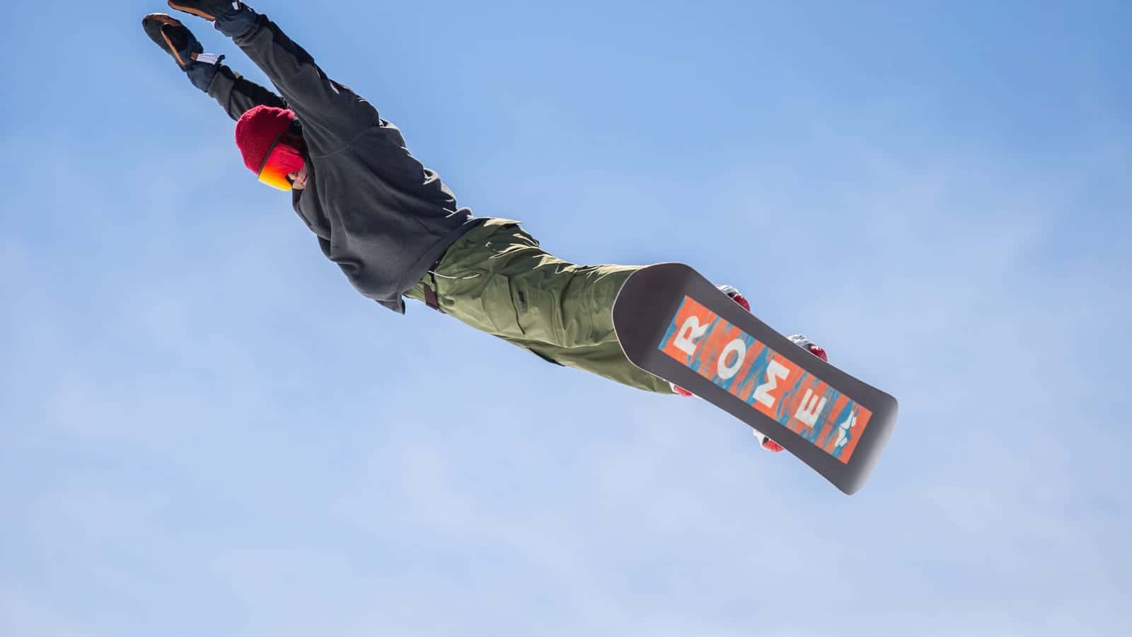 A snowboarder in mid-air against a blue sky, arms stretched out