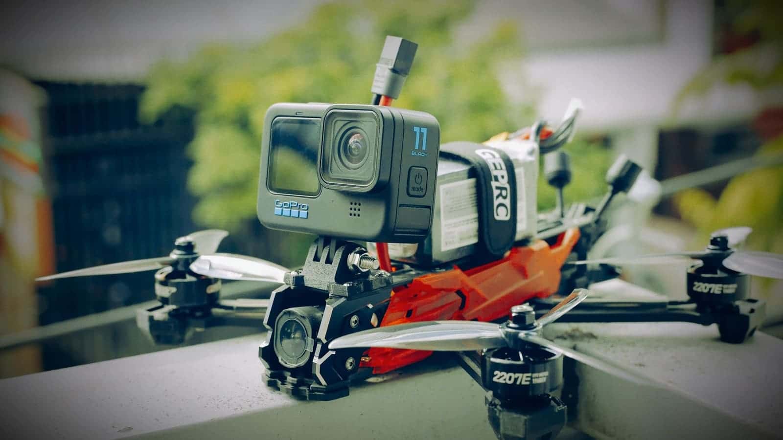 An FPV racing drone with an action camera strapped on top, resting on a ledge
