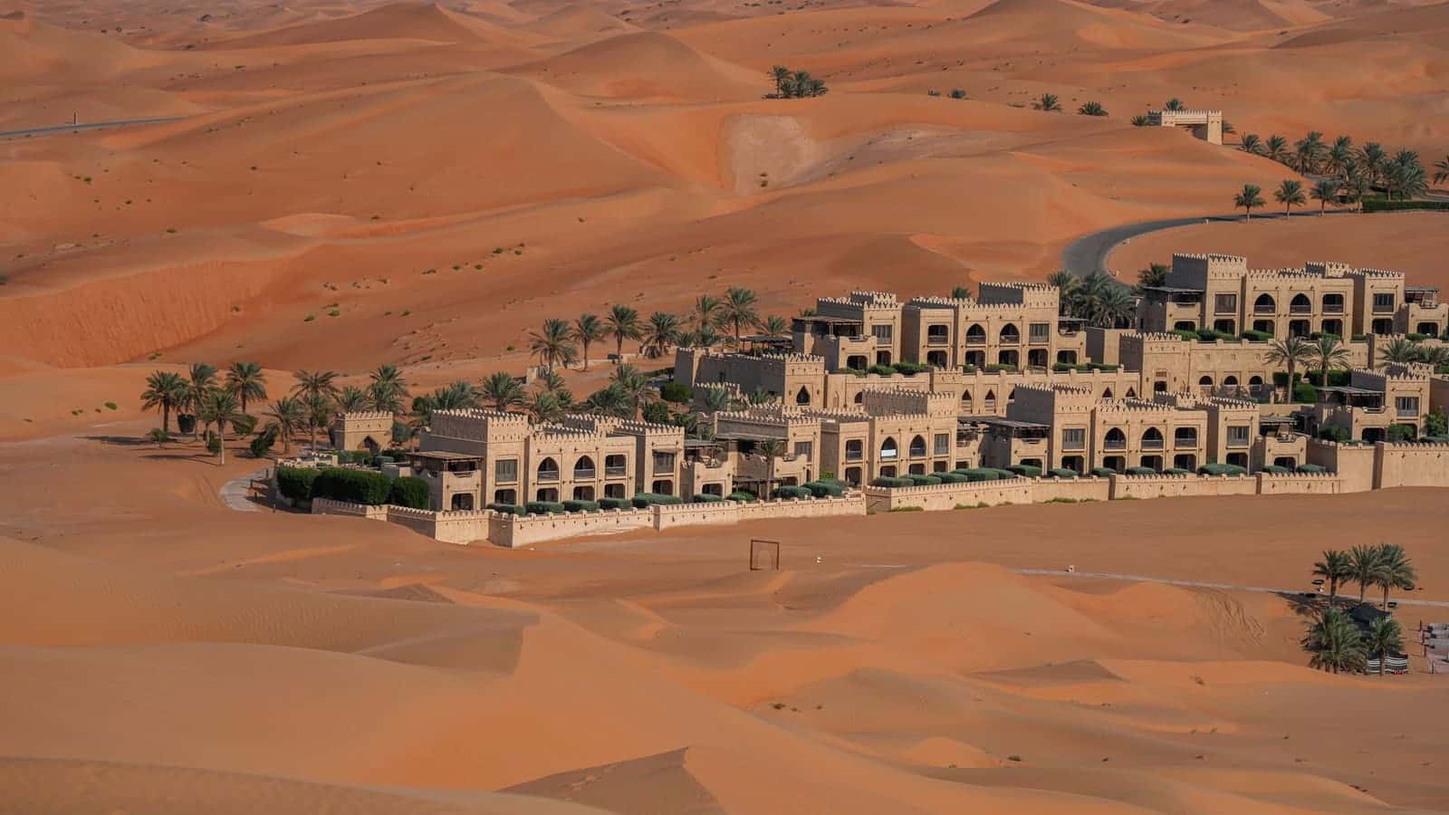 Aerial view of a sandstone desert resort with palm trees among the sand dunes