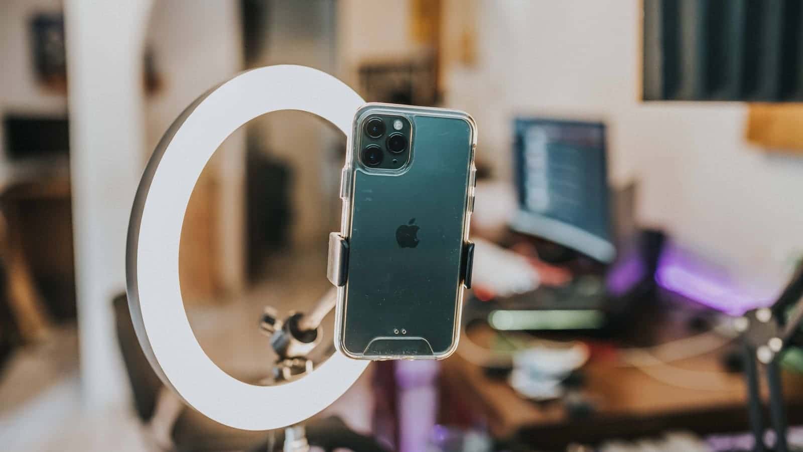 A smartphone clamped in a ring light on a desk, set up to film a vertical video